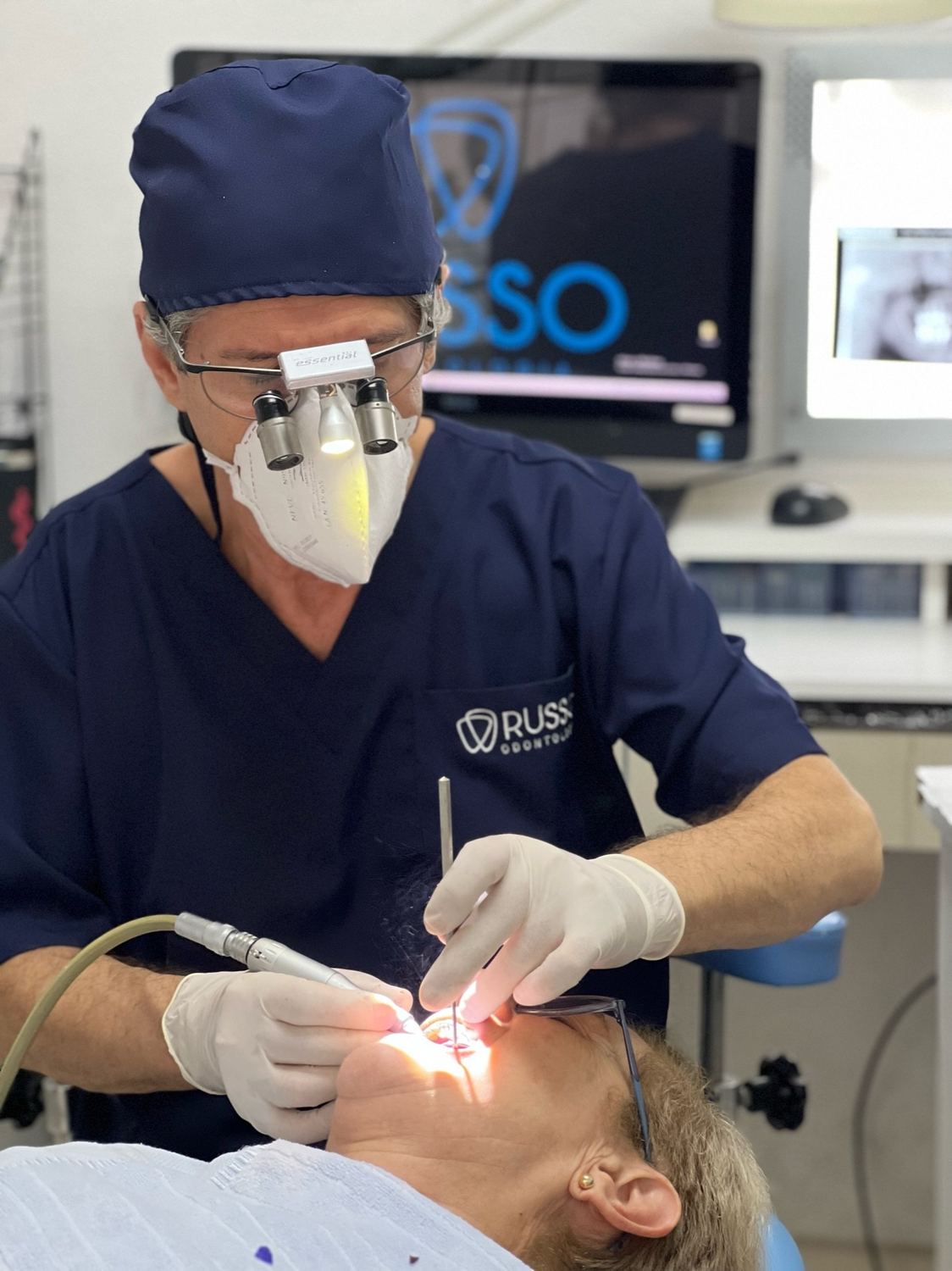 Dr. Carlos Russo em atendimento, com lupas cirúrgicas
