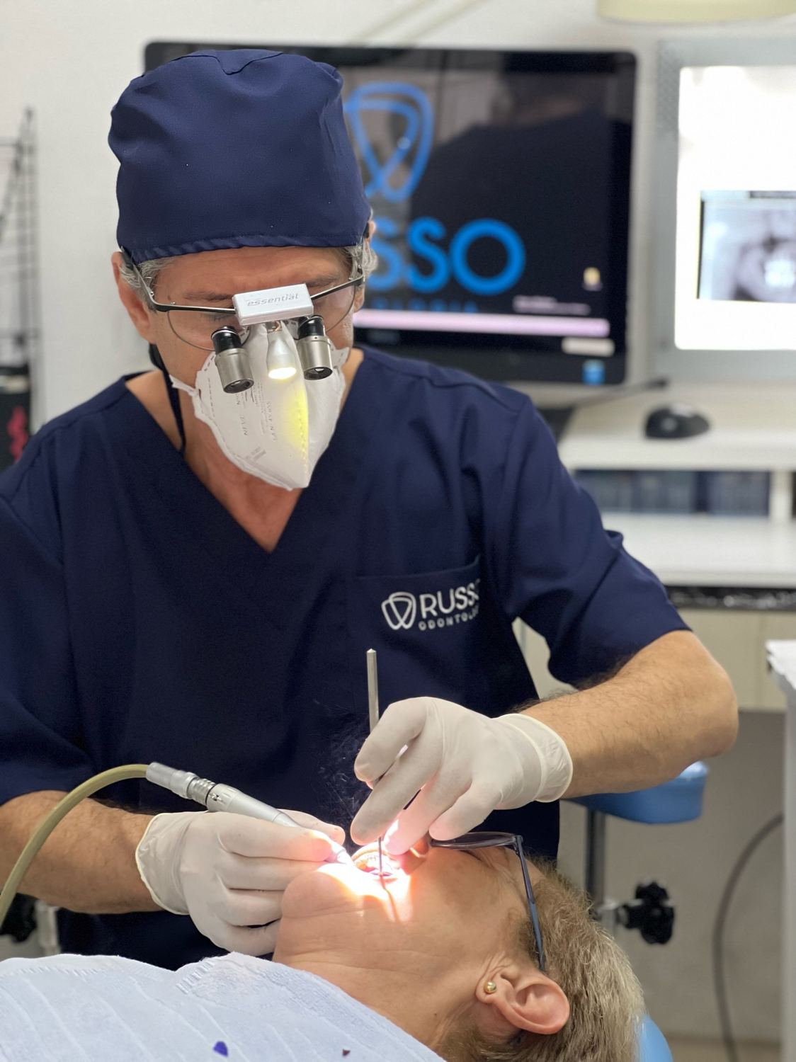 Dr. Carlos Russo em atendimento, com lupas cirúrgicas, no consultório da Russo Odontologia